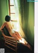 A naked woman sitting in a chair by a window.