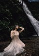 A woman in a white dress standing in front of a waterfall.