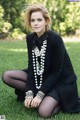 A woman sitting on the grass wearing a black dress and pearls.