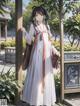 A woman in a long white dress standing in front of a tree.