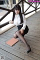 A woman in a white shirt and black skirt sitting on a wooden floor.