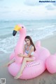 A woman sitting on an inflatable flamingo on the beach.